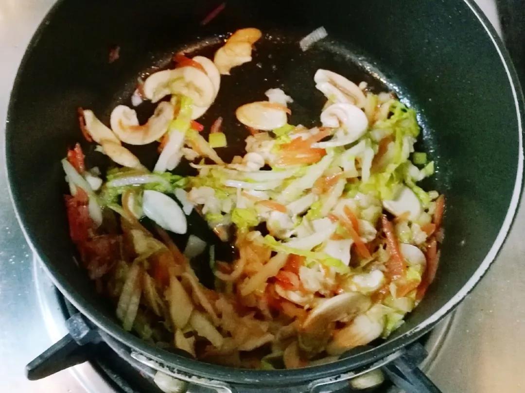 第4步：热锅入油，加入胡萝卜、口蘑翻炒变软，加入葱碎、贝柱和娃娃菜翻炒一会儿。