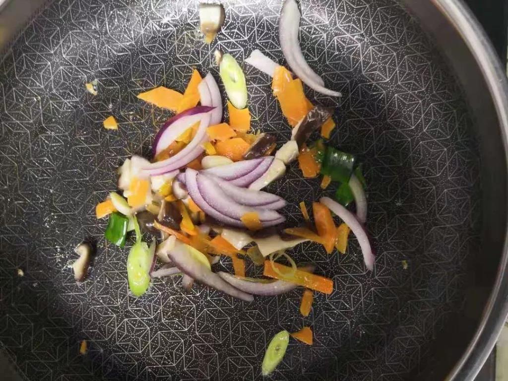 第6步：锅内倒入油，将葱花爆香，再加入胡萝卜、香菇、洋葱下锅煸炒。