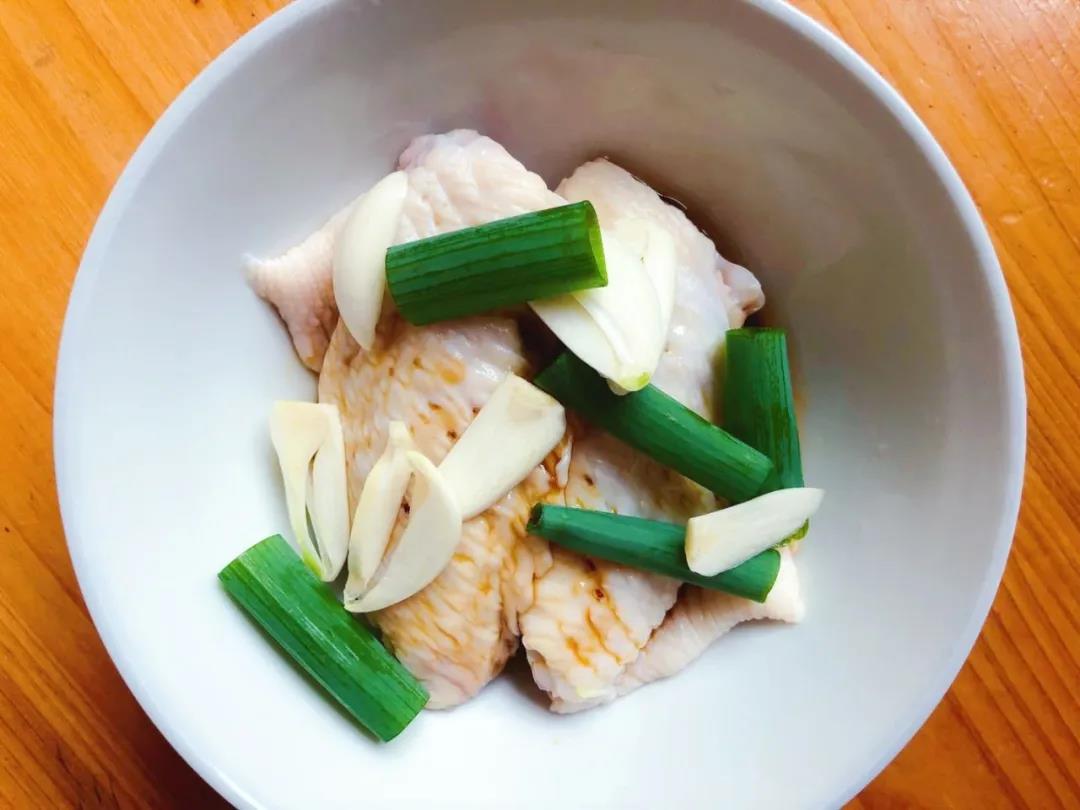 第5步：大蒜、葱段、芝麻油和生抽加入鸡翅，抓匀腌制20分钟。