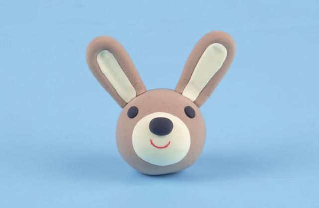 步骤3：把耳朵粘到头上，然后眼睛鼻子一一粘好，嘴巴部分事先用淡黄色粘土打个底，最后用红色笔画出小嘴巴