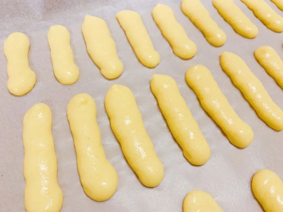 烤盘平铺油纸。裱花袋顶部剪一个小口，在油纸上挤出一条条的形状。