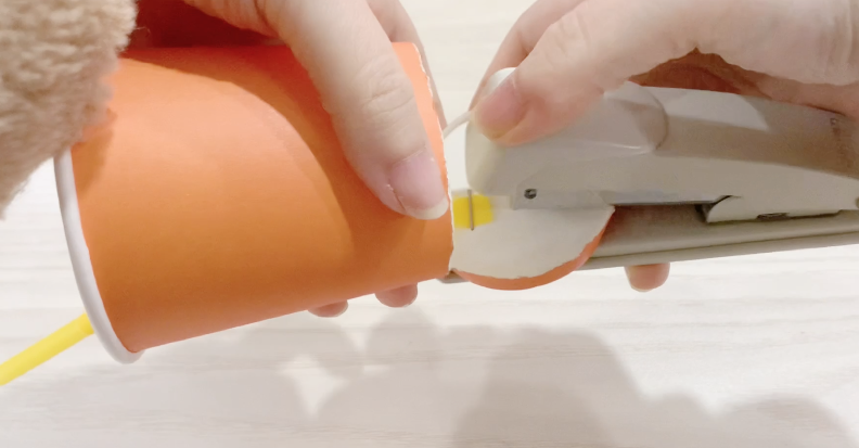 步骤4：用订书机把吸管跟底部的盖子订在一起。