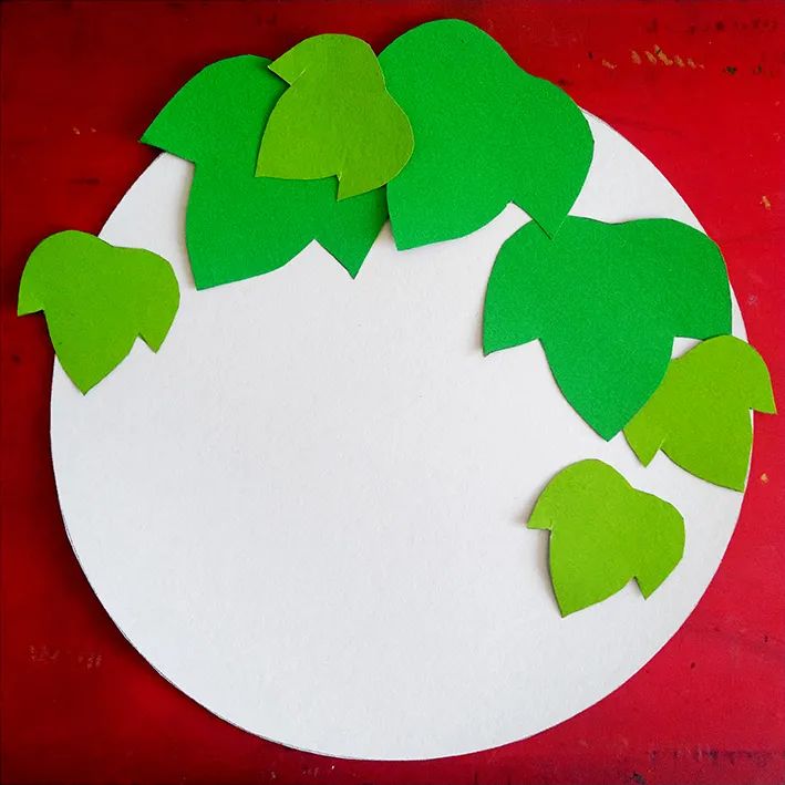步骤1：首先我们在白色圆形卡纸上，摆放绿色的叶子，也就是经营构图，此步骤不粘贴，只摆放，可调整，每个人也可以有不同的摆放方式，只要注意整体的构图的疏密即可。
