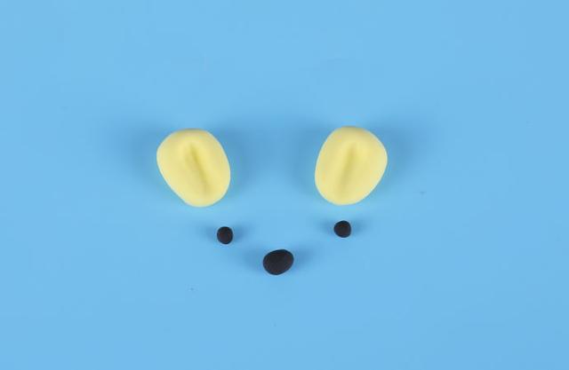 步骤6：柠檬黄色粘土做两只小耳朵，黑色粘土做出眼睛和鼻子，如上图所示。