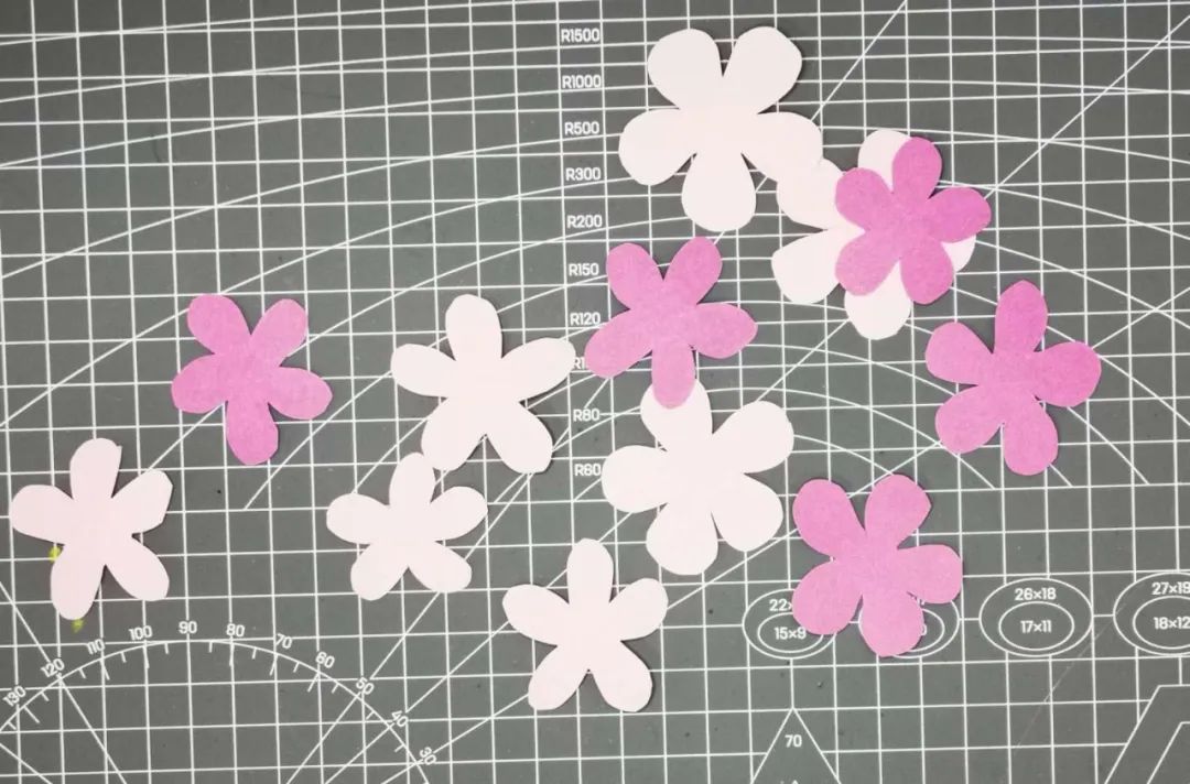 步骤1：选深浅不同的粉色的彩纸，画出简单的桃花造型后用剪刀剪下。可以将几张纸叠加在一起剪，这样能更方便快捷。