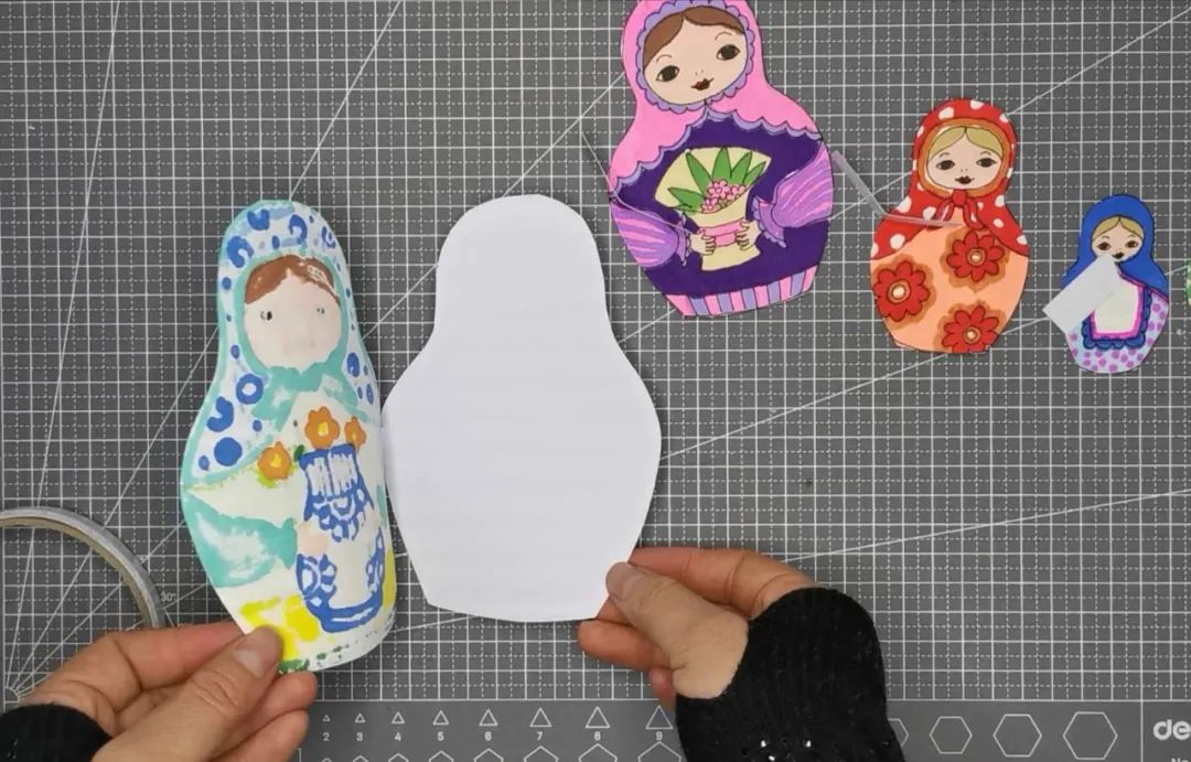 步骤6：小纸条一半粘在套娃上一半粘在空白纸上面，如下图一样。再把剩余的三个套娃按照从大到小的顺序用同样的方法粘好。最小的一个背后贴双面胶直接粘上即可。