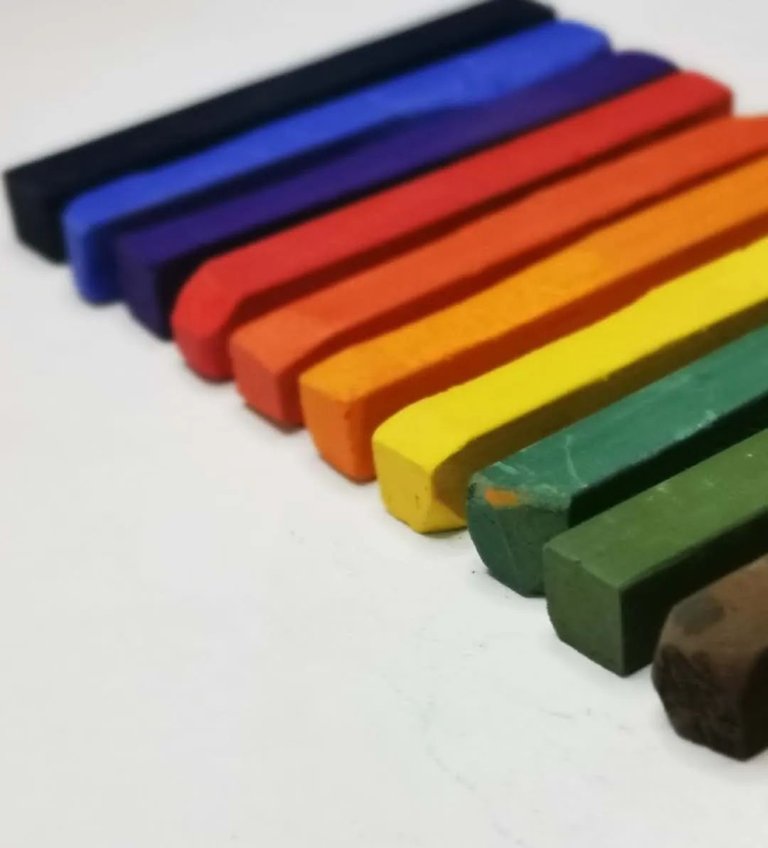 步骤1：铅笔在画纸下方画出地平线。如下图所示，按照棕色、橄榄绿、深绿、黄色、桔黄、桔红、红色、紫色、蓝色、深蓝的顺序准备好色粉笔，用美工刀分别将色粉笔刮出粉末在白色画纸上。使用小刀的时候要注意安全哦！