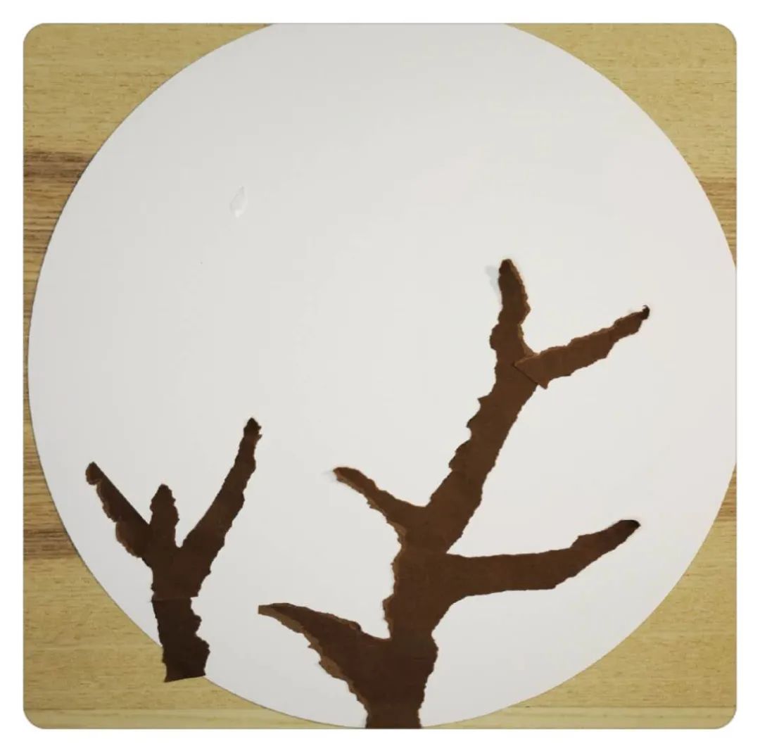 步骤1：先准备一张棕色的纸和一张圆形的白纸以及双面胶。将棕色的纸手撕出枝杈的形状，贴在白色纸上。可以从下向上长出枝子，也可以从侧面伸出。